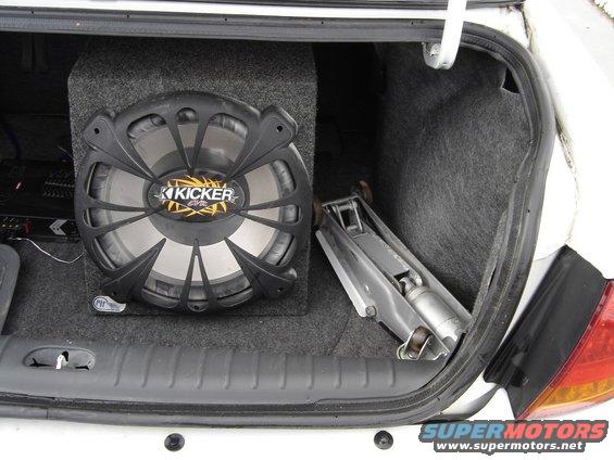 Car trunk showing a Kicker subwoofer box and a car jack. The trunk lining is grey carpet