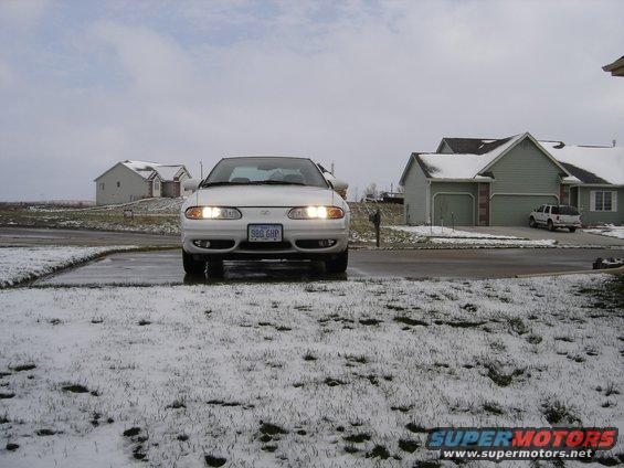 White sedan with headlights on, parked in a snowy driveway. License plate reads '986 GHP'