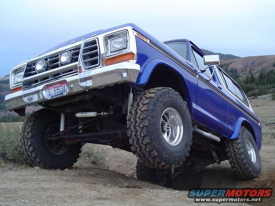 Blue 1978 Ford Bronco with lifted suspension and off-road tires driving on a dirt path