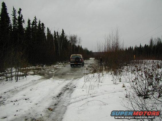 Tan SUV driving on a snowy, icy road through a forest