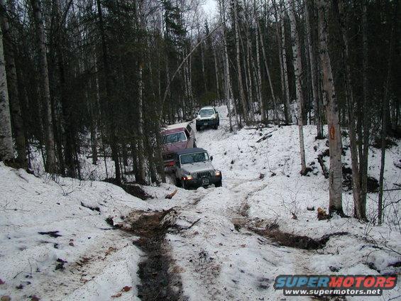 Three SUVs navigate a muddy and snowy path through a dense forest