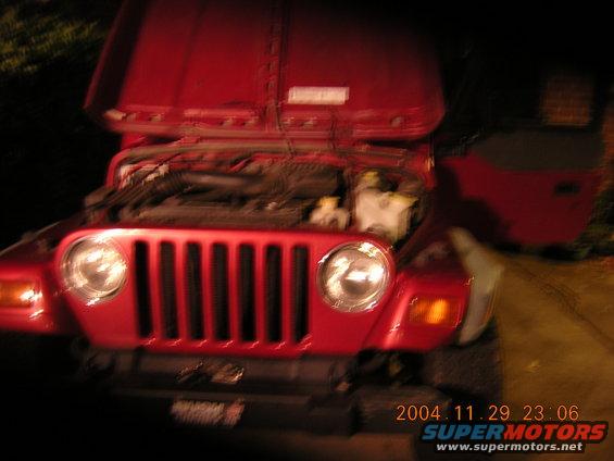 Red Jeep Wrangler with hood open, showing engine. Front grille and headlights visible