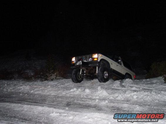 White SUV with aftermarket bumper and large tires on a snowy incline at night