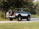 1994 Ford Bronco - This lifted Ford Bronco is shown from the rear, parked on a paved surface with grass and trees in the background.