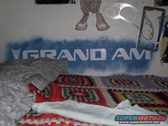 Wall art with "GRAND AM" text and a Pontiac logo, above a bed with blankets
