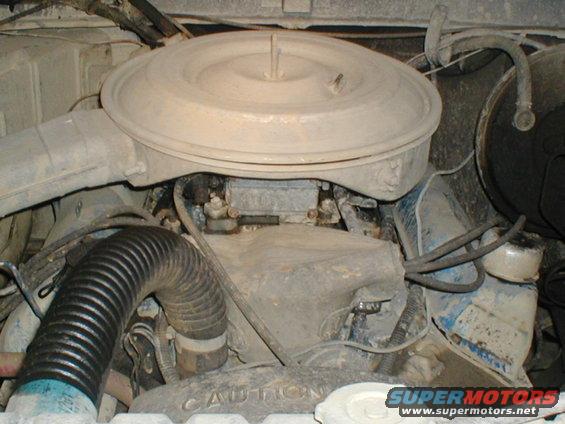 Engine bay with a large, dusty air filter housing over a carburetor. A black ribbed hose is visible on the left