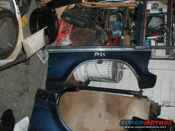 Dark blue car fender with chrome trim and 'PASS' written in white marker. A fan is visible inside the wheel well