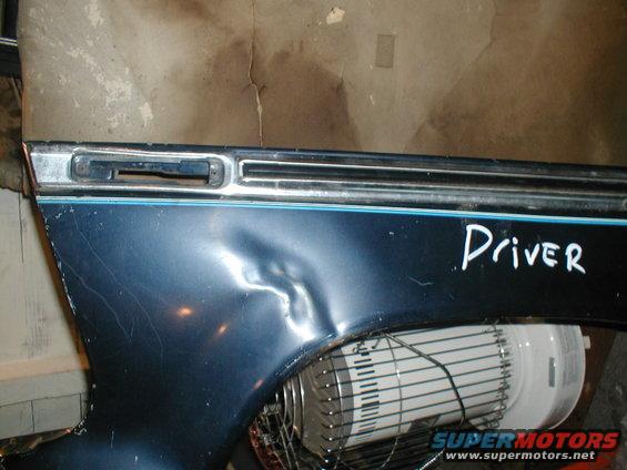 Blue vehicle fender with a large dent and "Driver" written on it