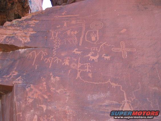 Ancient petroglyphs on a rock face, showing figures, animals, and symbols