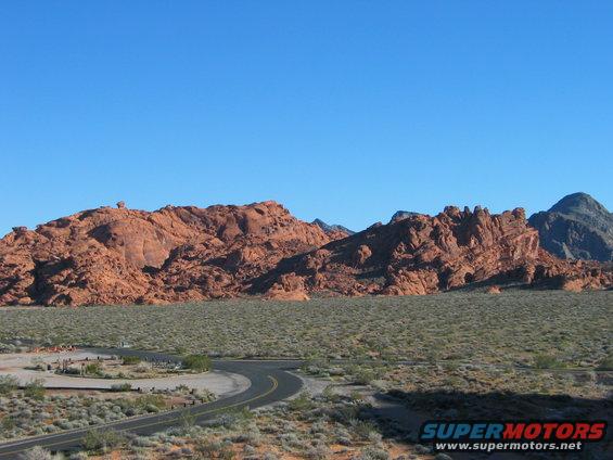 Desert landscape with red rock formations and a winding road under a clear blue sky