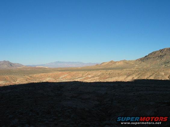 Desert landscape with mountains under a clear blue sky, a large shadow covers the foreground