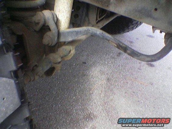 Close-up of a vehicle's suspension and tire, showing a bent metal bar and part of a tire