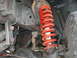 1994 Ford Bronco - The front suspension system of a vehicle, a bright red coil spring and various metal components.