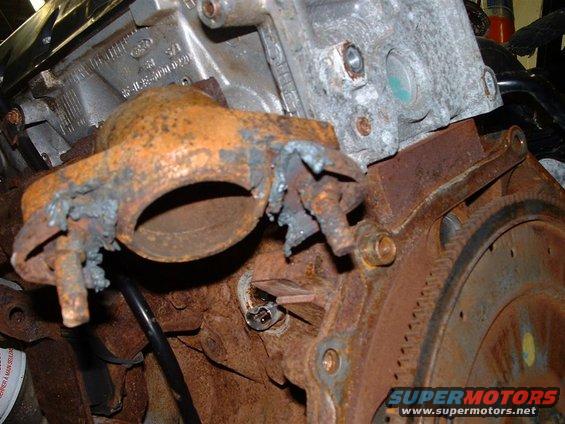 rusted exhaust manifold bolted to a corroded engine block with visible Ford casting marks