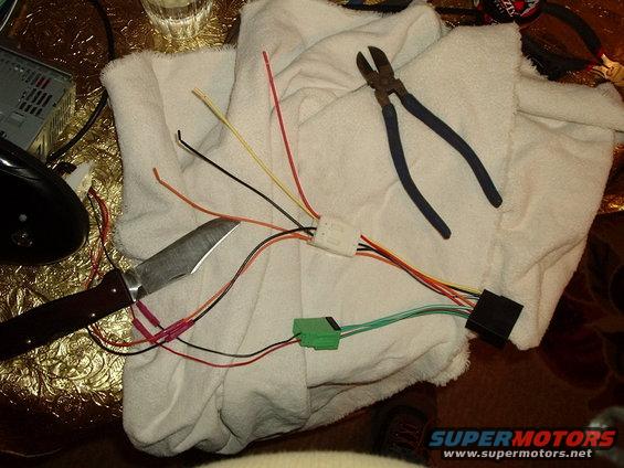 Car stereo wiring harness with cut wires, a knife, and wire cutters on a towel
