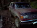 1988 Ford Bronco - This red Ford Bronco is navigating a challenging off-road path through a wooded area.
