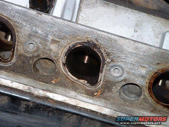 Close-up of a dirty engine cylinder head exhaust port with carbon buildup