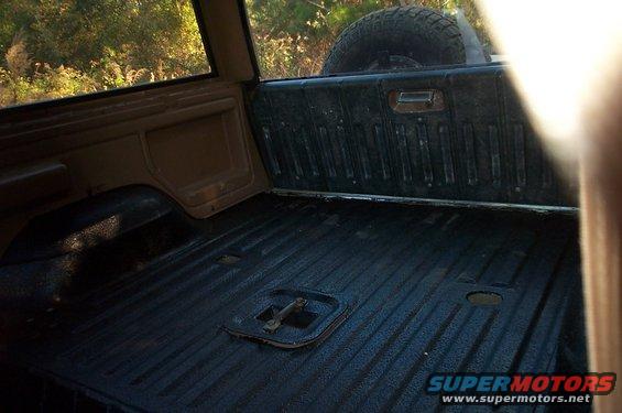 Rear cargo area of an SUV, spare tire visible above. Textured floor with tie-down points