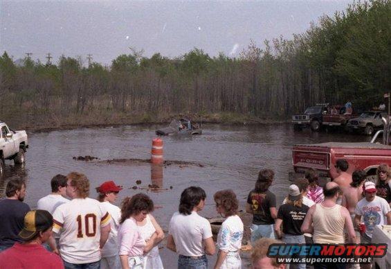 1991 Ford Bronco partially submerged in mud, with other trucks and people watching