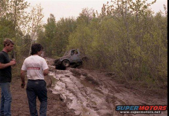 Suzuki Samurai stuck in mud on a trail with two guys watching