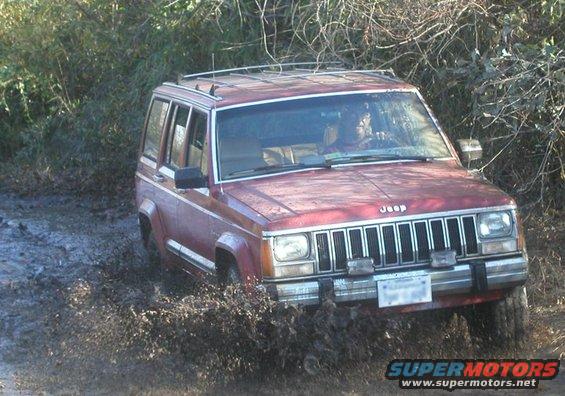 Red Jeep Cherokee XJ driving through mud and splashing water