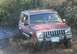 1988 Ford Bronco - A red Jeep Cherokee XJ navigates a muddy trail, kicking up a significant amount of dirt and water.