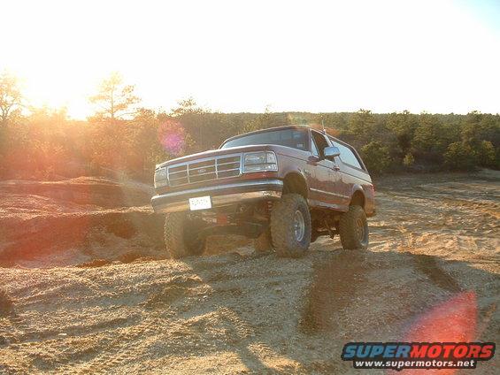 Red SUV with lifted suspension on a dirt hill, front grille visible