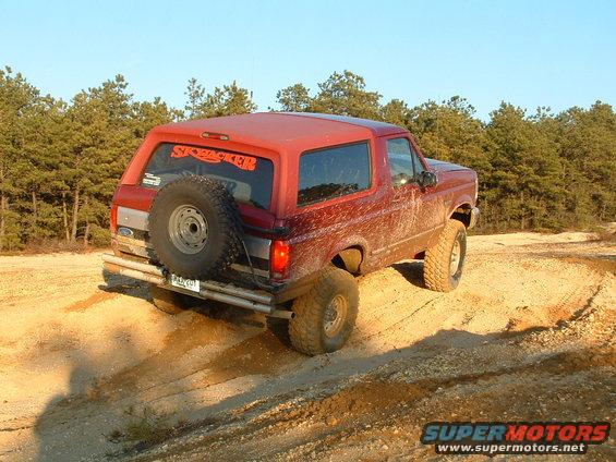 Red SUV with spare tire on rear, driving on dirt trail. 'SKYPACKER' sticker on rear window