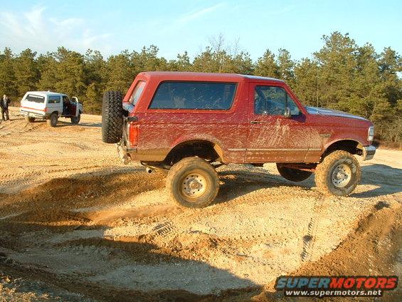 Red Ford Bronco with a spare tire on the rear door, lifted suspension, and mud splatters, parked on a dirt track