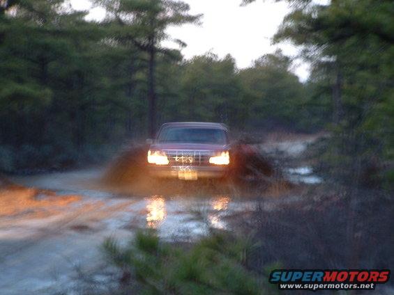 Red 1989 Chevrolet Blazer driving through a muddy trail, kicking up water