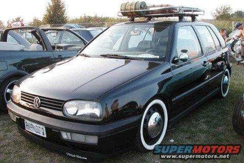 Black Volkswagen Golf hatchback with whitewall tires and a roof rack carrying cylindrical objects