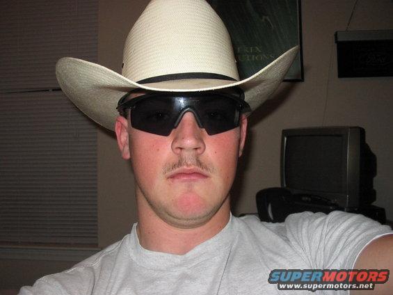 Man in cowboy hat and sunglasses, light gray t-shirt, with a small mustache