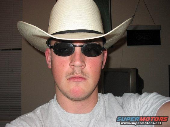 Man in cowboy hat and sunglasses, Ford logo on wall