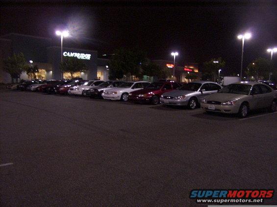 Several sedans parked in a lot at night, with a building in the background