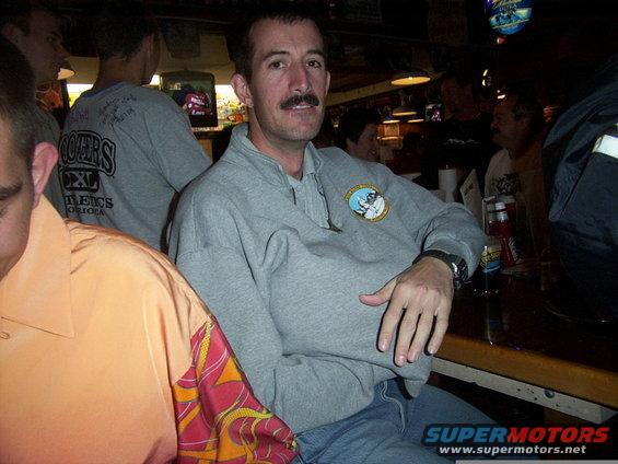 Man in gray sweatshirt with mustache sitting at a bar