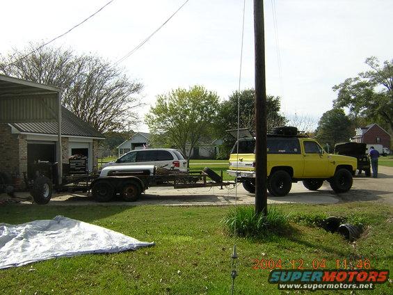 Yellow SUV with roof rack and spare tire, towing a trailer. Visible damage on the front of the trailer