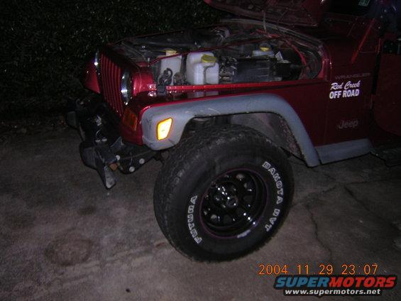 Front corner of red Jeep Wrangler, hood open, showing engine bay. "Red Creek OFF ROAD" sticker on fender