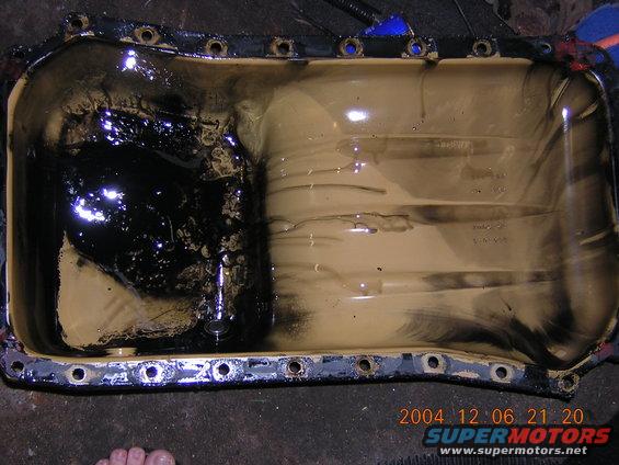 Dirty oil pan with sludge on one side and tan residue on the other. Some numbers are visible inside