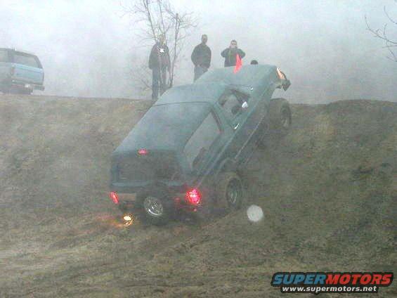 Dark green SUV tilted on a muddy hill, rear taillights illuminated