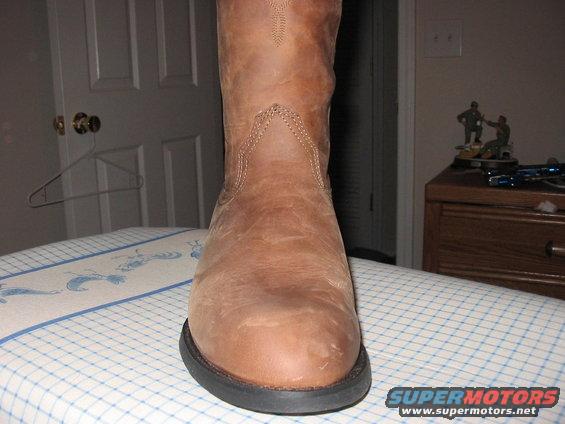Brown leather cowboy boot on a checkered surface, with a door and nightstand in the background