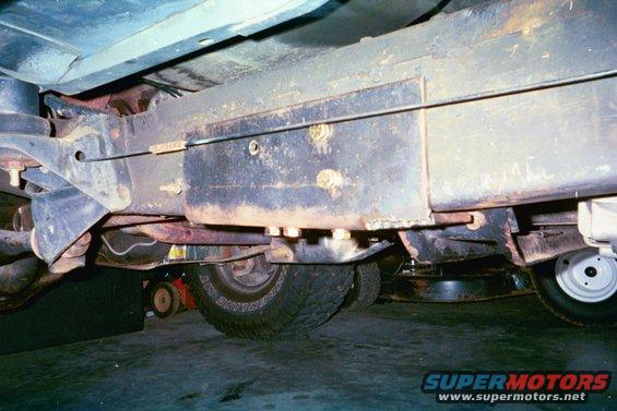 Underside view of a vehicle's frame and suspension components, showing rust and some bolted-on parts