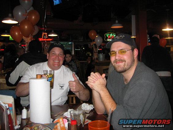 Two men smiling at a table with balloons and Budweiser sign