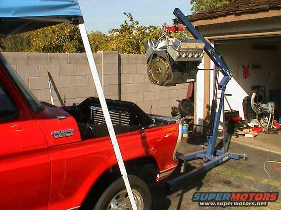 Red Ford Bronco with hood open, engine being lifted out by a blue engine hoist