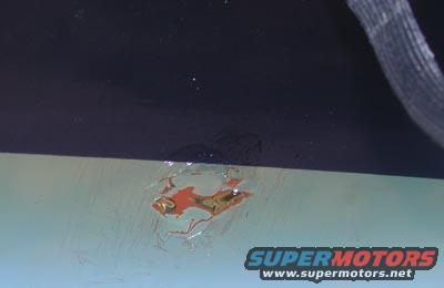 Close-up of chipped paint on a car, showing rust underneath. Supermotors.net logo visible