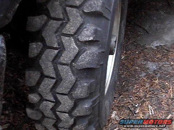 Close-up of a knobby off-road tire on a vehicle. The tread pattern is aggressive, suitable for dirt or mud