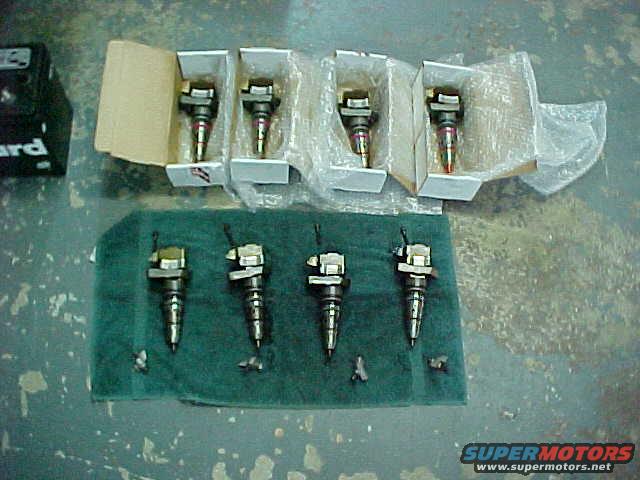 Five fuel injectors laid out on a green cloth, with four more in boxes