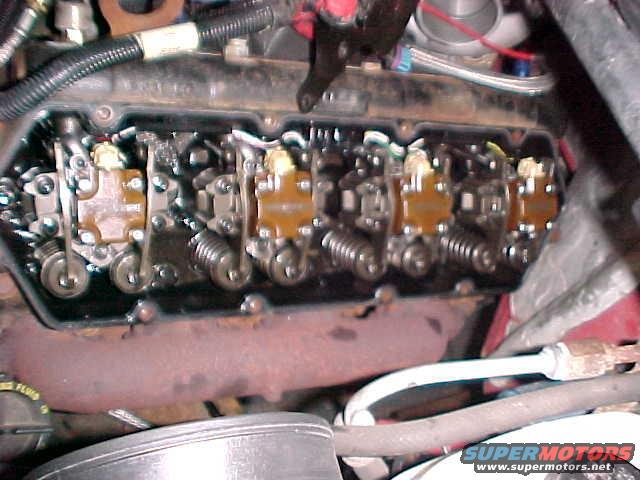 Engine valve train with visible springs and rockers. Rusty exhaust manifold below