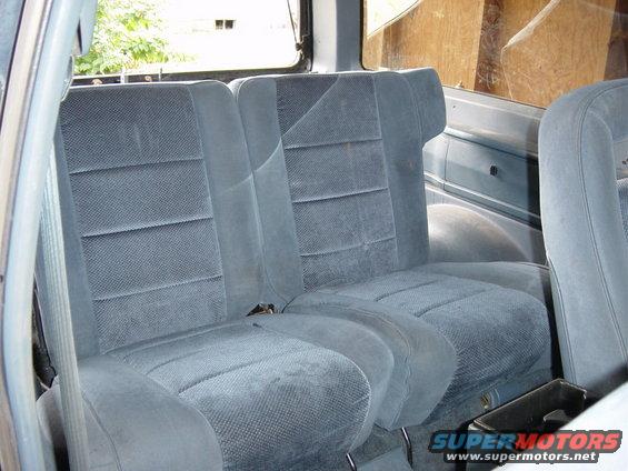 Back seats of a vehicle, blue fabric upholstery, visible seatbelts and interior panels
