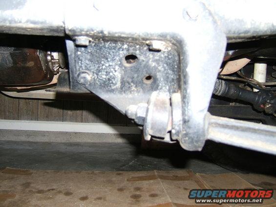 Close-up of a vehicle's suspension linkage and bracket, showing bolts and metal components