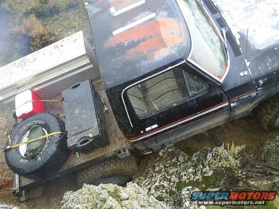 Truck with flatbed loaded with a spare tire, cooler, and toolbox, driving off-road